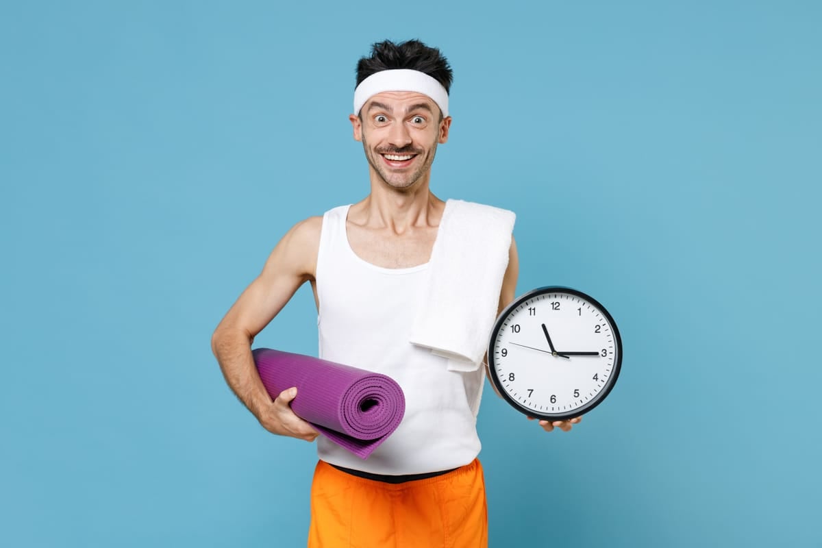 Man holding clock, towel, and yoga mat ready to work out