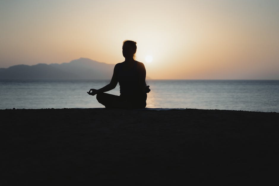 A woman doing yoga on a beach with the sunset in the background